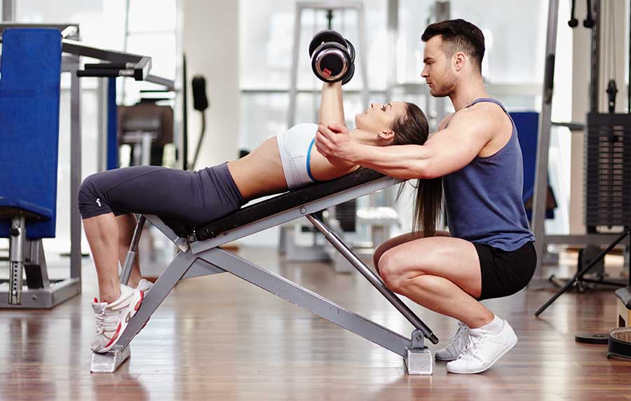 male personal trainer assisting a woman with her chest press form in a gym