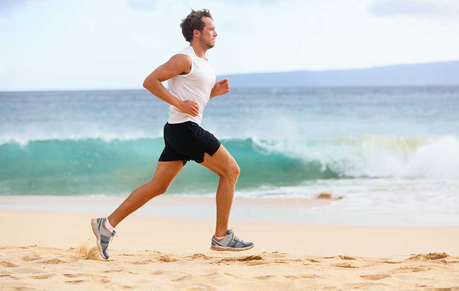 man in white tank top and black shorts running on the beach